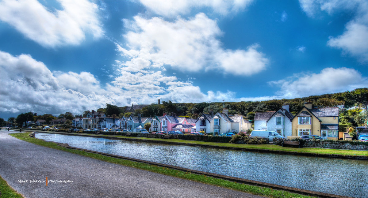 Row of colourful houses along a riverbank under a partly cloudy blue sky.