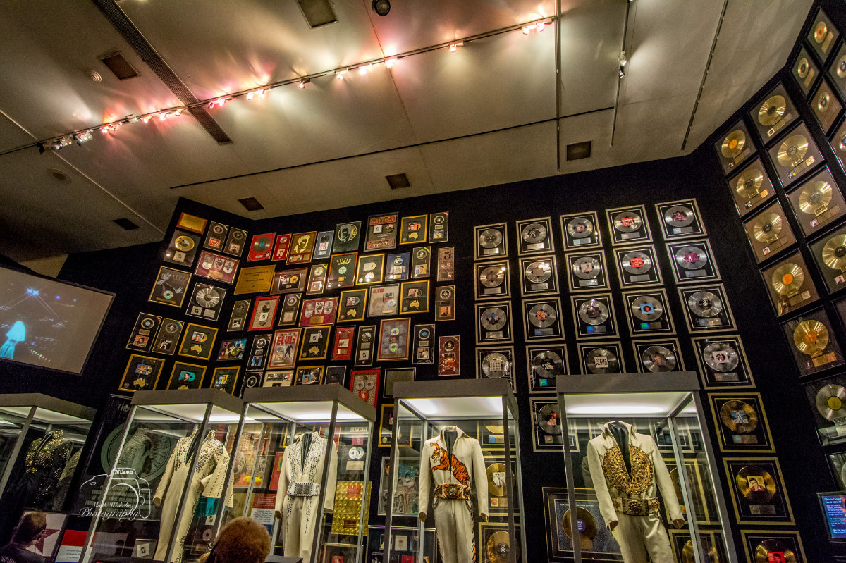 Exhibit displaying iconic sequined jumpsuits in glass cases beneath walls covered with framed gold and platinum music records.