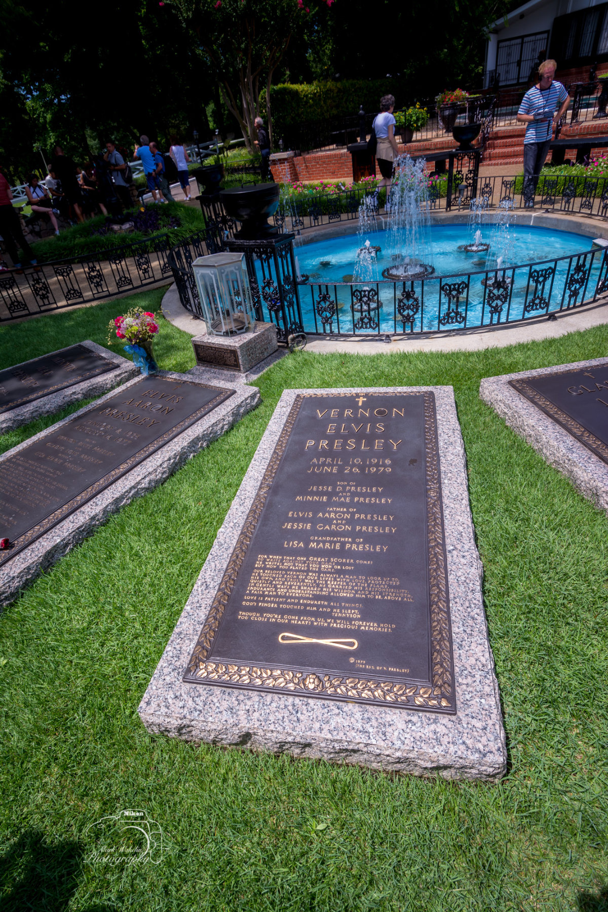 Gravestones of Vernon Elvis Presley and Elvis Aaron Presley near a decorative fountain surrounded by a black wrought iron fence in a garden.