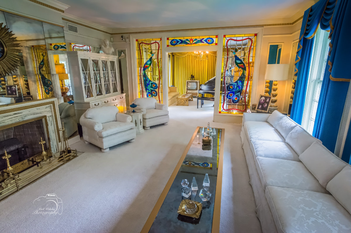 Luxurious living room with white sofas, stained glass peacock panels, a grand piano, and yellow curtains in the background.