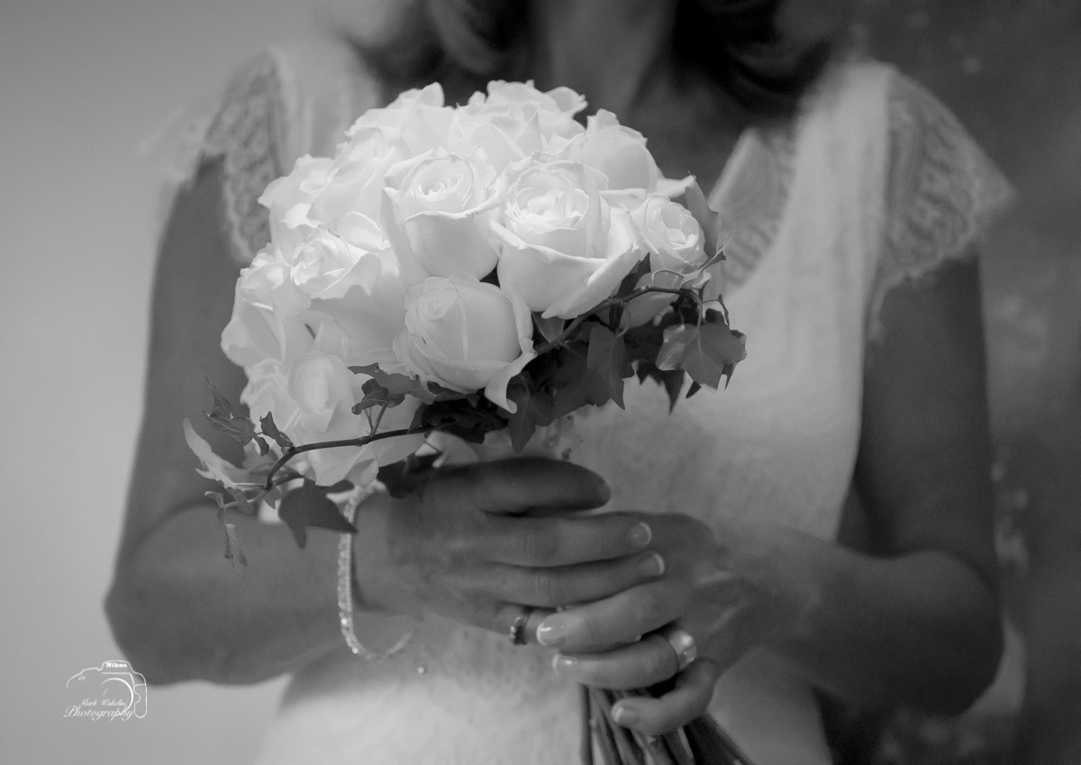 Close-up of a woman in lace dress holding a bouquet of roses with visible rings on her fingers.