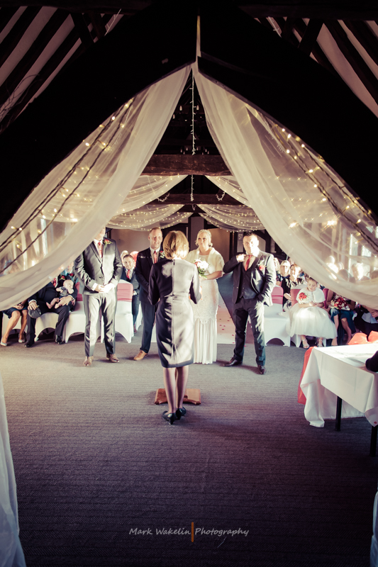 Bride and groom standing at the altar with the officiant during a wedding ceremony inside a decorated venue with draped fabric and string lights.
