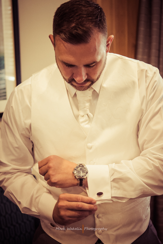 Man in a white waistcoat and tie adjusting his cufflink.