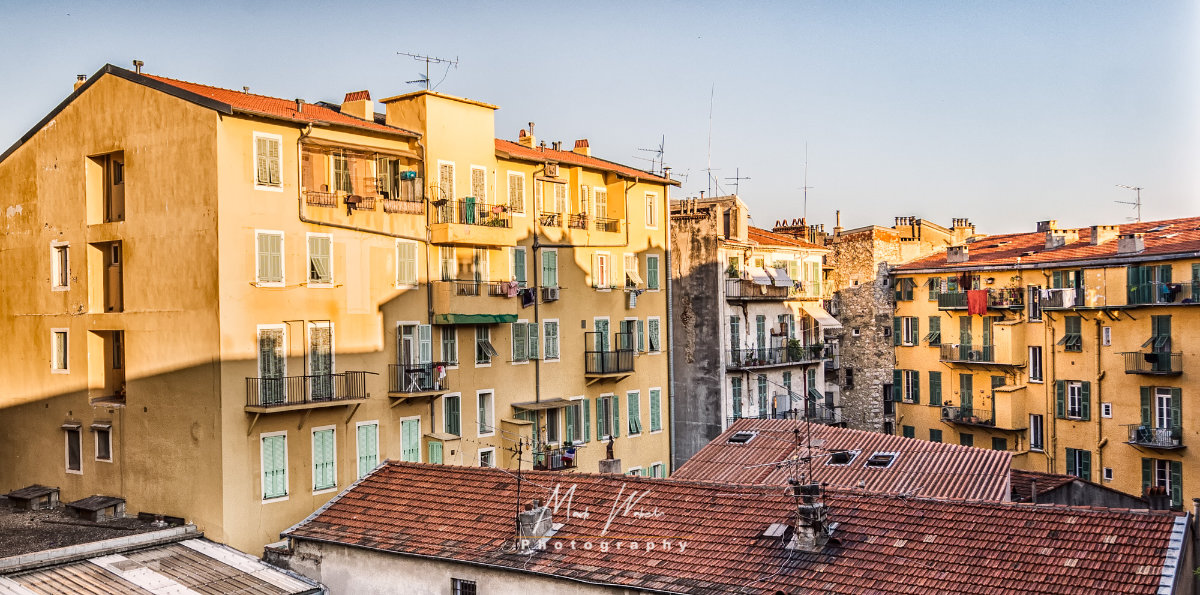 Yellow residential buildings with green shutters and balconies under clear sky in the golden hour.