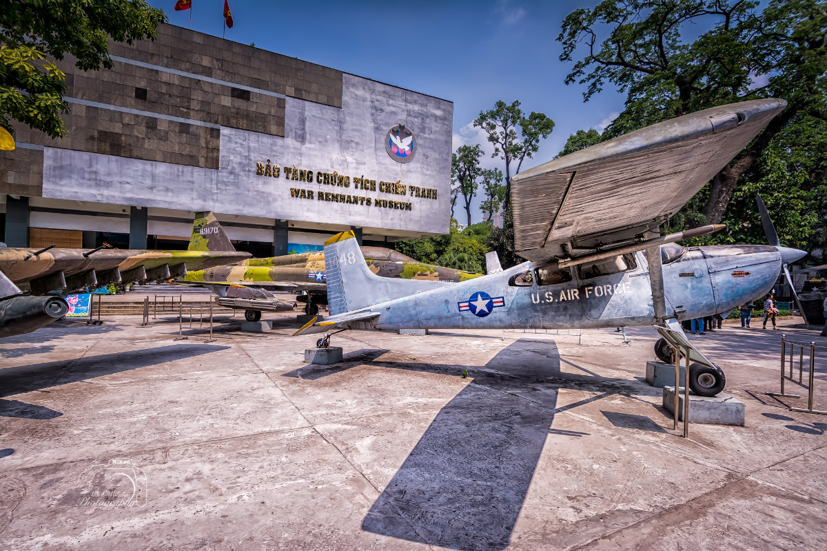 Outdoor display of vintage military aircraft including a U.S. Air Force plane in front of the War Remnants Museum building in Saigon.