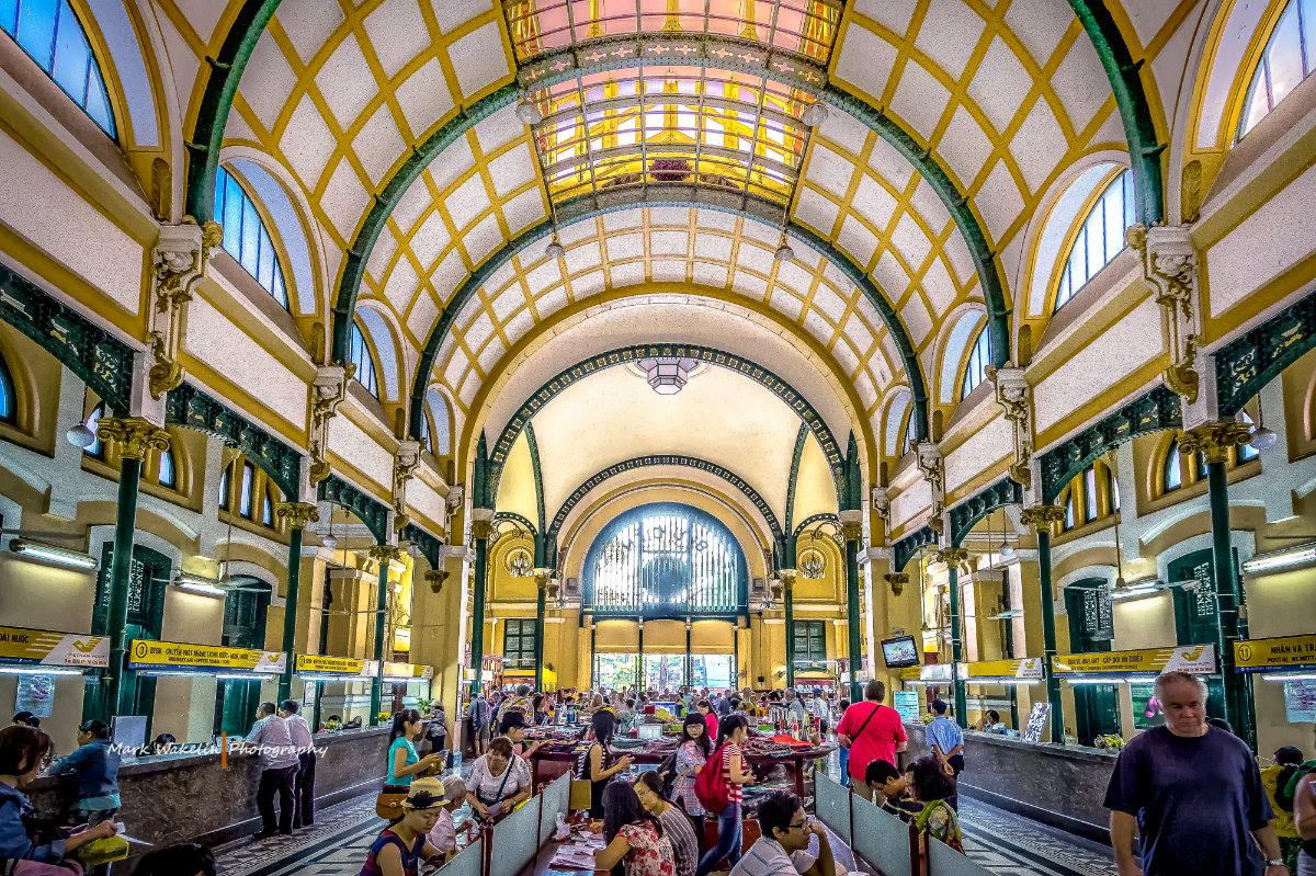 Interior of Saigon Central Post Office with yellow arched ceiling and people inside.