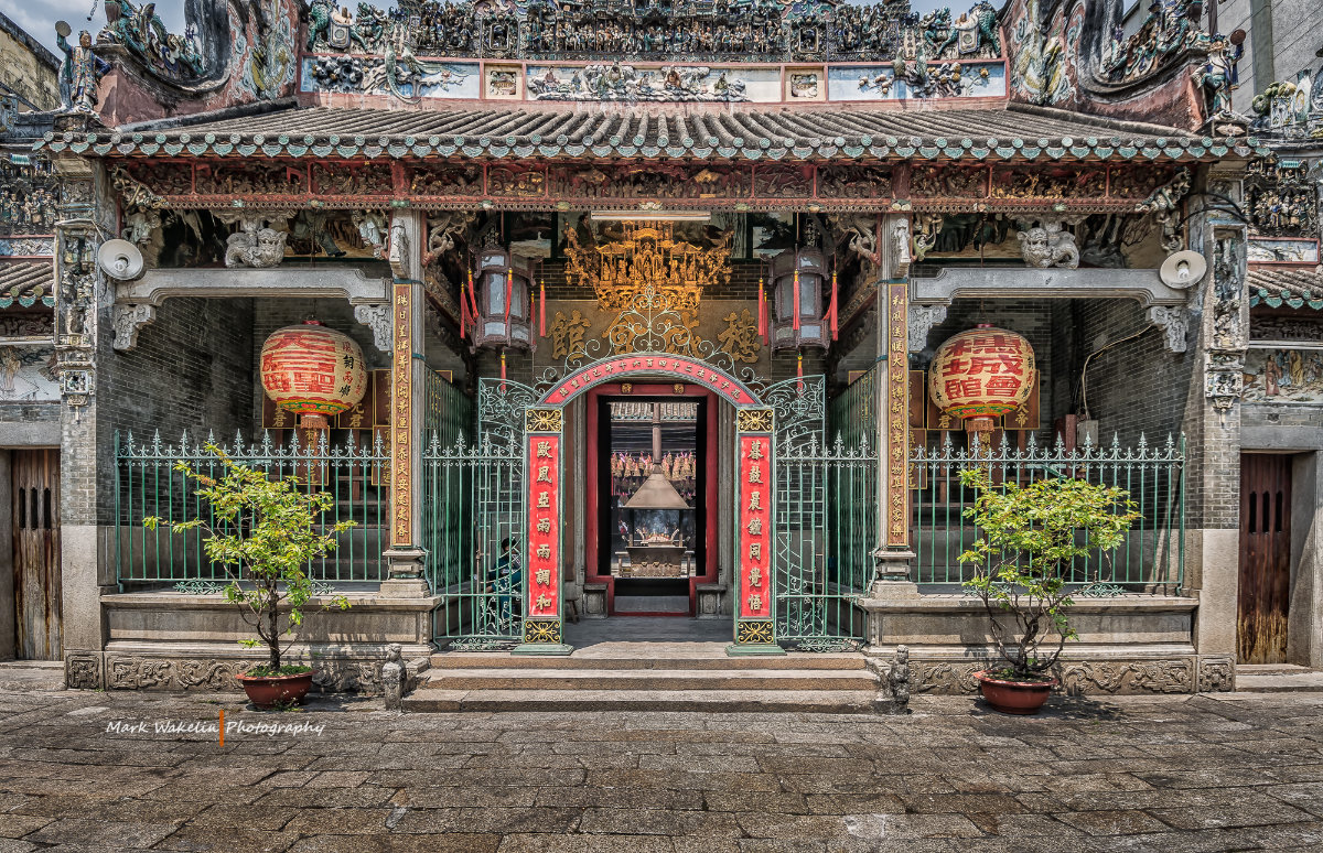 Decorative entrance of a traditional Chinese temple with red lanterns, intricate roof carvings, and potted plants.